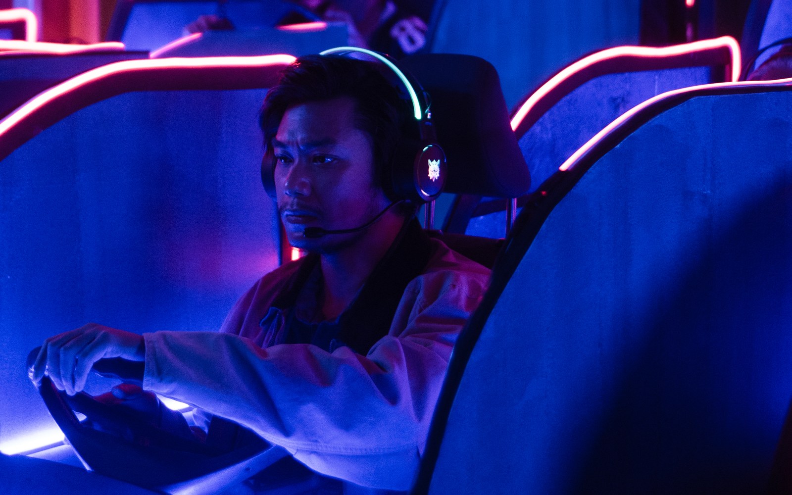 John wearing a headset, hand on a wheel, focused