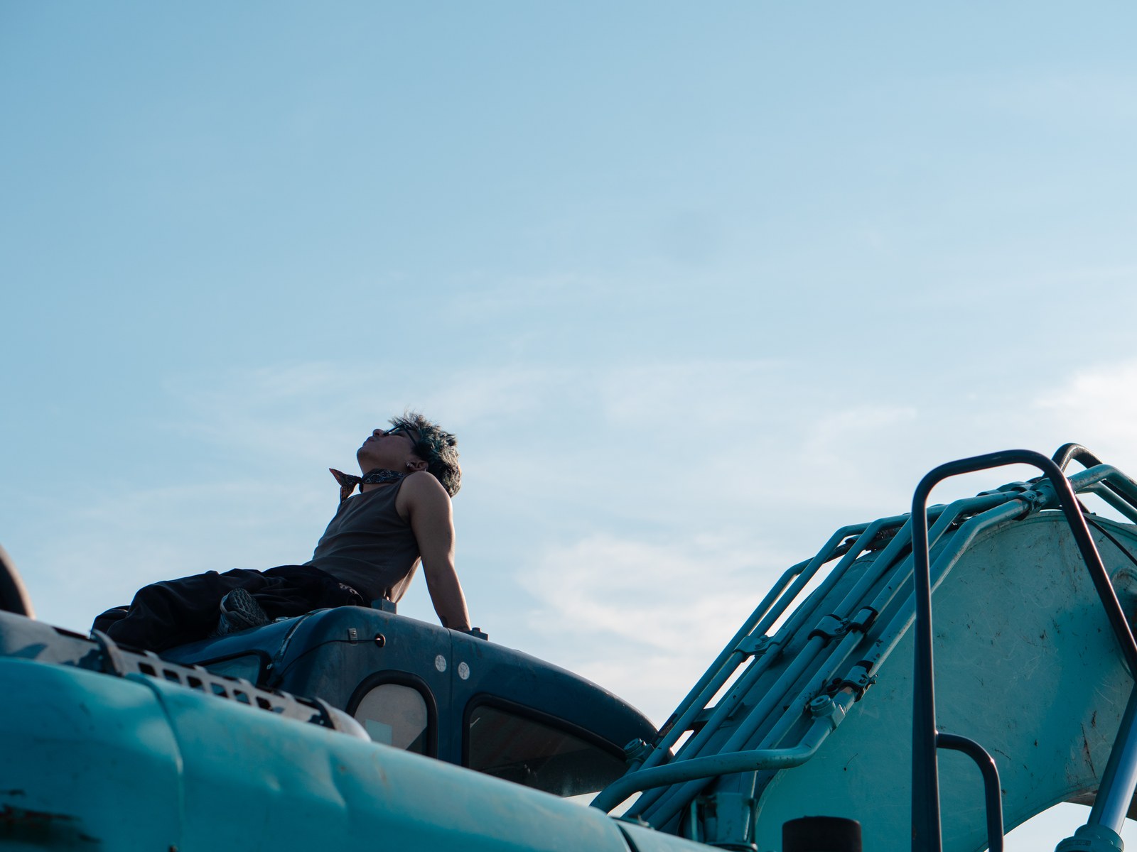John lying atop equipment on set, looking up at the sky
